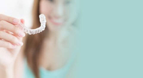 Clear dental aligner held by smiling woman